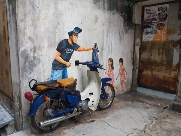 Man With Scooter Handing Bag To Children - Mural Art In Ipoh